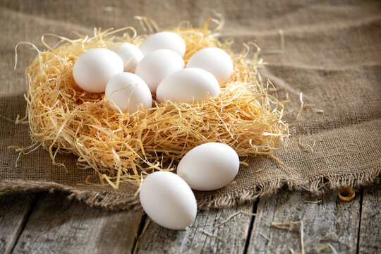 White chicken eggs in the straw nest on a burlap on wooden boards