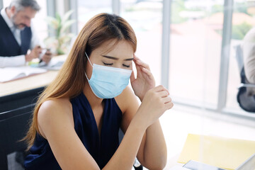 Young Asian businesswoman wearing mask preventing for Covid corona virus and have a headache and...