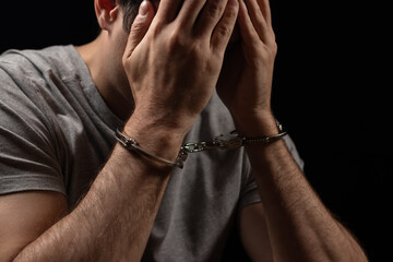 Handcuffed man covering his face with his hands. Arrested and handcuffed criminal man with handcuffs - obrazy, fototapety, plakaty
