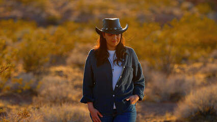 A fearless cowgirl, adorned in a rugged cowboy hat, strides through the harsh desert landscape of...