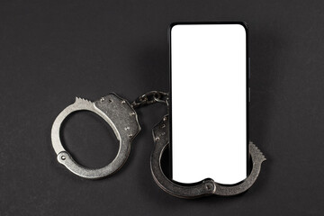 mobile phone with handcuffs and white screen, the concept of dependence on gadgets and digital...