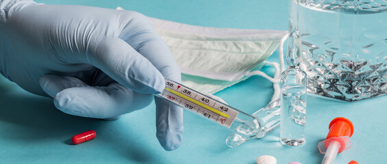 doctors hand in blue latex glove holding thermometer indicating high temperature. Healthcare and...