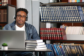 In modern classroom African-American student wearing headphones is studying online on laptop,...