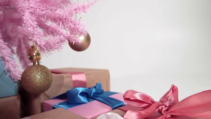 Pile of wrapped boxes are under pink New Year fir decorated with golden balls filmed in closeup on white background. Celebrating traditional winter holidays with glamour Christmas tree and gifts
