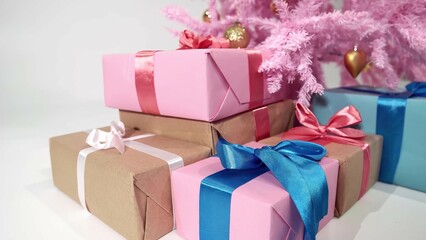 Isolated footage of gift boxes pile lying under festive Christmas tree filmed in closeup on white background. View on plenty of presents with ribbons next artificial New Year fir of pink colour