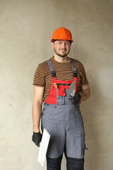 Smiling repairman in overalls and protective orange helmet holds two spatulas for plastering concrete wall with putty using. Repair work at apartment and construction new building concept. Copy space