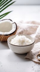 Close-up of coconut oil in a white bowl, with coconuts and wooden spoon, on a neutral surface.