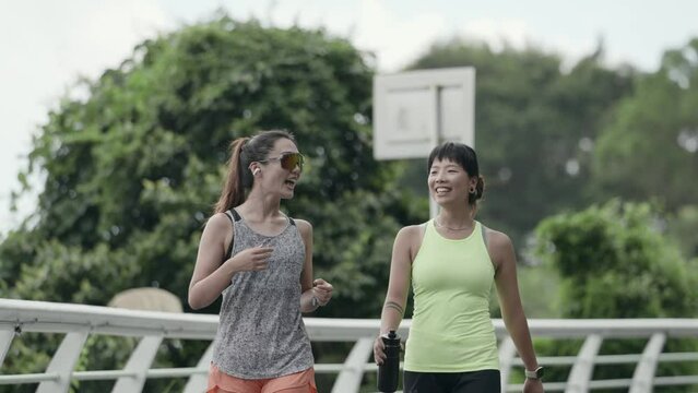 two happy young asian women walking chatting in park while exercising outdoors