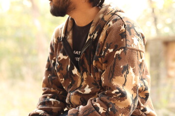 An Indian boy wearing brown camouflaged jacket and jeans while sitting on the marble bench,...