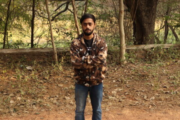 An Indian boy wearing camouflaged jacket with green trees and vegetations in the background