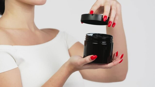 Hands of a young woman holding a container with body and skin care cream. Organic cosmetic product isolated on white background. Advertising and skin care concept.