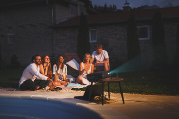 Friends having fun watching a movie in a backyard open air cinema