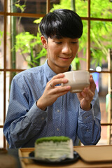 A Vertical image of young Japanese man looks at matcha tea in a traditional Japanese earthenware...