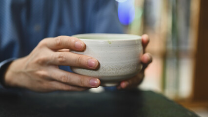Close-up and cropped image of a man's hands holding a Japanese traditional matcha tea cup, Matcha...