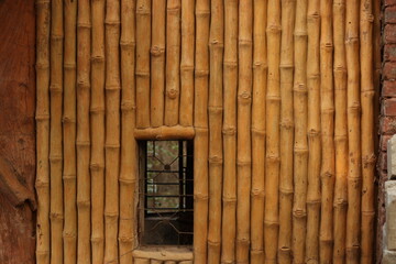 A Wall made up of dried brown bamboos with a hole for a gate