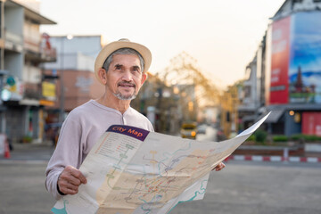 attractive asian senior pensioner with grey hair and beard,older adult man tourist wearing hat,standing at the crossroads by the street,using a paper map to search tourist attractions in the city