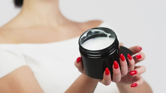 Hands of a young woman holding a container with body and skin care cream. Organic cosmetic product isolated on white background. Advertising and skin care concept.