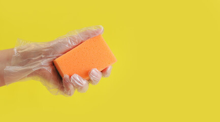 Orange dishwashing sponge in a woman's hand on a yellow background. A hand in a transparent...