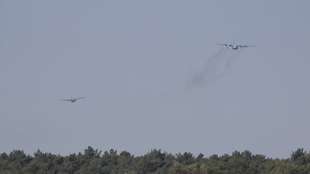 two military aircraft flying low over the forest trees towards the camera. Lockheed C-130 Hercules and Transall C-160.