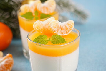 Panna cotta with tangerines jelly and mint, Italian dessert, homemade cuisine. On the background are branches of a green Christmas tree.