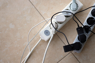 Overloaded power boards. Power strips with different electrical plugs on white floor. Concept of...