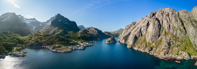 Sweeping drone panorama of Nusfjord, highlighting the serene blue fjord flanked by steep mountains,...