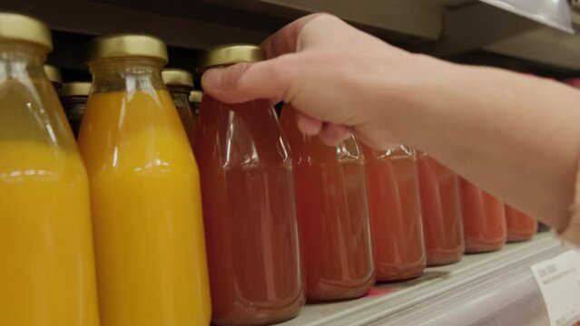 Buyer chooses juice drink in glass bottle on grocery supermarket shelf close-up.