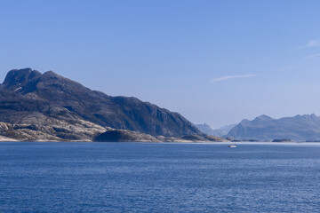 A picturesque view of the North Sea with a solitary, sculpted mountain towering over tranquil waters, featuring a sailing boat near Lofoten Island