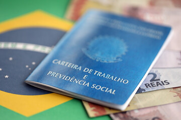 Brazilian work card and social security blue book and reais money bills on flag of Federative...