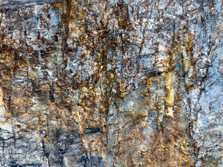 Close up of a cave rock face with various colors and textures. The rock is predominantly brown and yellow with patches of white and black. The texture is rough and jagged.