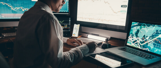 Close-up male trader analyzing stock market while sitting at office workstation with computers