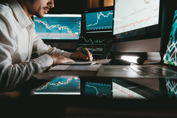 Close-up male trader analyzing stock market while sitting at office workstation multiple computers