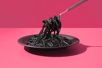 Espaguetis con tinta de calamar negro en un plato con tenedor sobre fondo rosa	