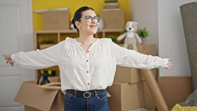 Young beautiful hispanic woman smiling moving around new house with open arms at new home