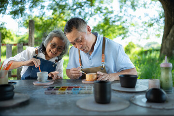 In the pottery workshop, an Asian retired couple is engaged in pottery making and clay painting...