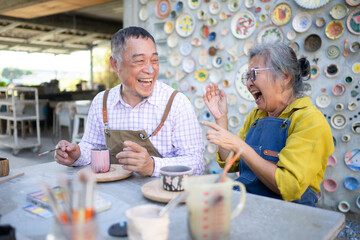In the pottery workshop, an Asian retired couple is engaged in pottery making and clay painting activities. - Powered by Adobe