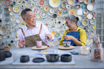 In the pottery workshop, an Asian retired couple is engaged in pottery making and clay painting...