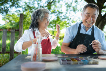 In the pottery workshop, an Asian retired couple is engaged in pottery making and clay painting activities.