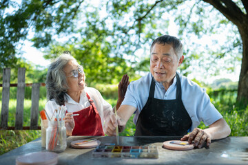 In the pottery workshop, an Asian retired couple is engaged in pottery making and clay painting activities.