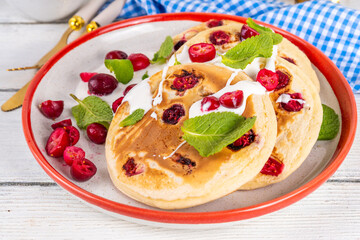 Sweet cranberry pancakes for winter breakfast or brunch. Festive Christmas, New Year breakfast dessert with vanilla creamy topping and fresh cranberries, copy space