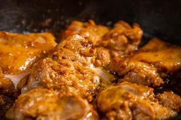 Chicken pieces in a sauce with spices are fried in a frying pan.