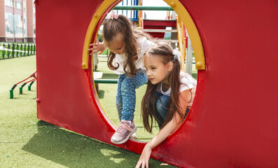 Two cute little girls on the playground. They play in the school yard. Concept of summer, fun, family and relaxation. Two sisters having fun outside