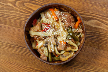Wok udon noodles with beef and vegetables in a coconut shell plate