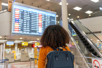Black woman looks at the flight schedule on a digital monitor in an airport to check the gate and...
