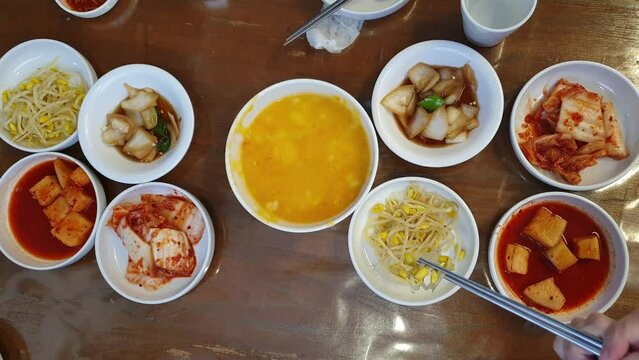 Hand eating Korean food banchan side dishes and Hobakjuk Pumpkin Porridge top view hands chopsticks