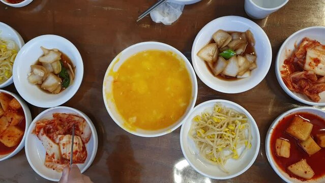 Hand eating Korean food banchan side dishes and Hobakjuk Pumpkin Porridge top view hands with chopsticks