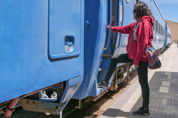 Side profile of a female tourist embarking a blue train carriage.  Vertical image