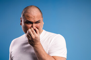 man with left hand holding his nose, feeling uncomfortable and looking to the side