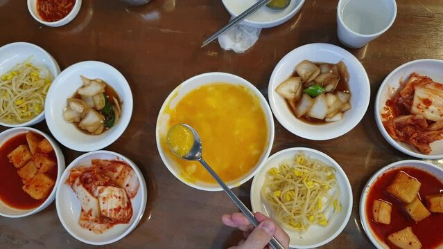 Hands eating Korean food banchan side dishes and Hobakjuk Pumpkin Porridge top view with chopsticks