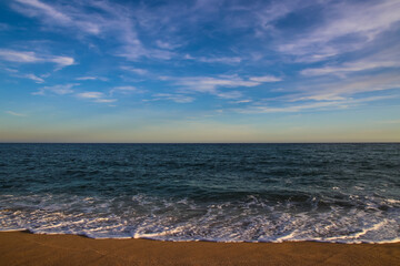 Vista del mar y la playa con luz de atardecer. Cielo azul con nubes dispersas.